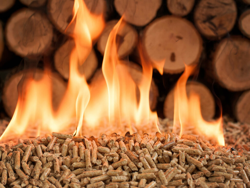 Brennende Pellets vor einem Holzstapel